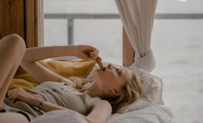 Donna stesa sul letto che mangia un biscotto