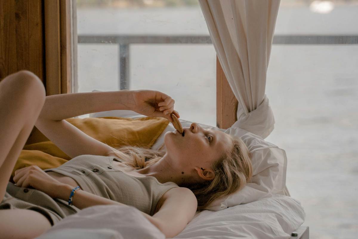 Donna stesa sul letto che mangia un biscotto