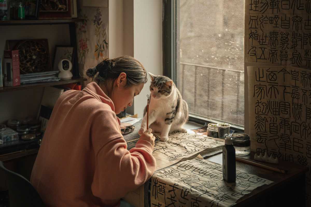 Ragazza che scrive su una scrivania con un gattino che le tocca la matita