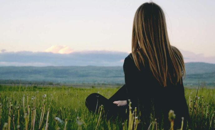 Ragazza seduta sull'erba che guarda l'orizzonte