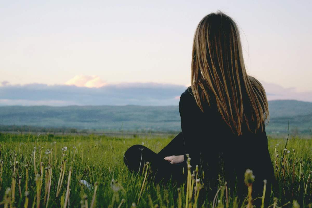 Ragazza seduta sull'erba che guarda l'orizzonte