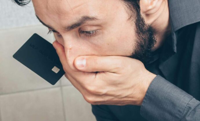 Uomo preoccupato con una mano sulla bocca e una carta di credito fra le dita