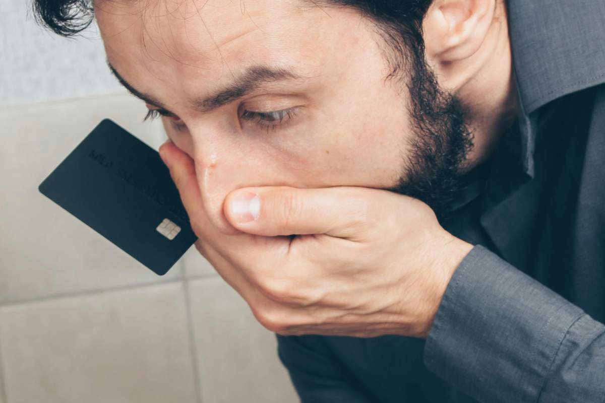 Uomo preoccupato con una mano sulla bocca e una carta di credito fra le dita
